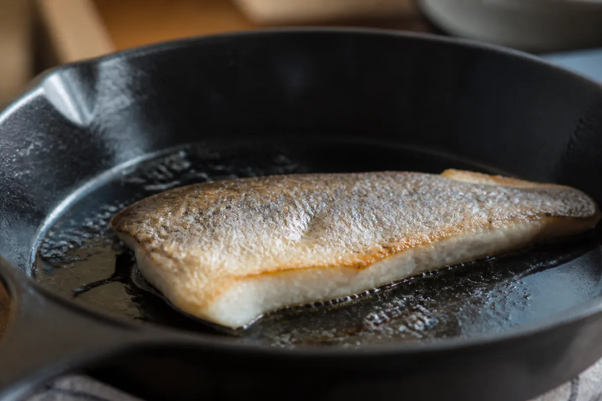 Filet de poisson blanc à peau argentée saisi dans une poêle en fonte avec un filet d&rsquo;huile d&rsquo;olive